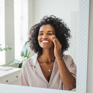 Attractive young woman cleaning her face with a cotton pad in the bathroom at home