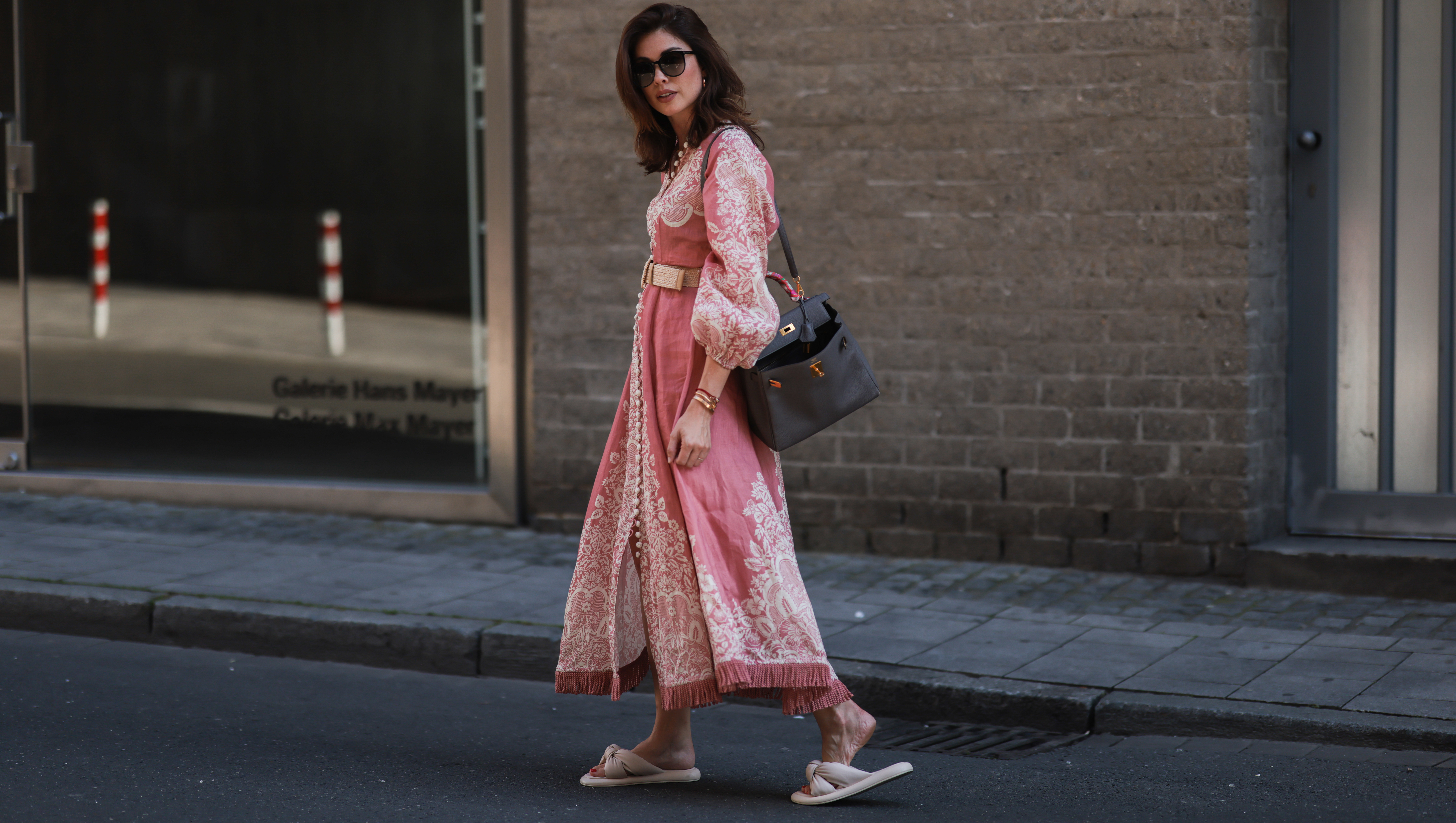 DUSSELDORF, GERMANY - JULY 24: Ira Meindl is seen wearing a rose, pink and white printed long Zimmermann dress with a beige belt, a black leather handbag from Hermes, black Saint Laurent sunglasses and beige Catwalk slipper on July 24, 2022 in Dusseldorf, Germany. (Photo by Jeremy Moeller/Getty Images)